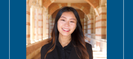 A young woman with long dark hair standing in the UCLA Royce Hall brick arches. She is wearing a black top.