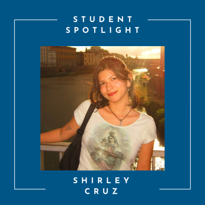 A young woman in a white tshirt standing with a river and sunset behind her