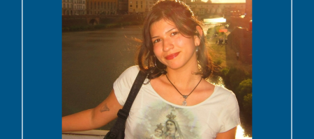 A young woman in a white tshirt standing with a river and sunset behind her