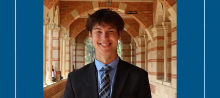 Young man in a dark suit, smiling, under the Royce Hall arches