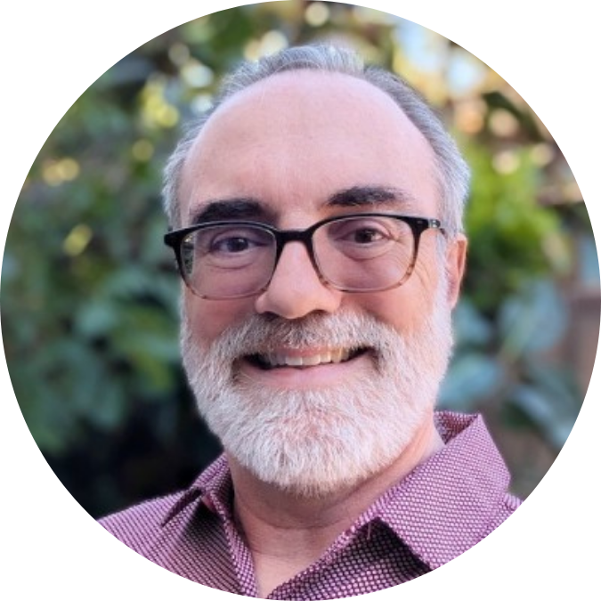 Jon Bassinger-Flores headshot Person with short gray hair, gray beard, glasses.